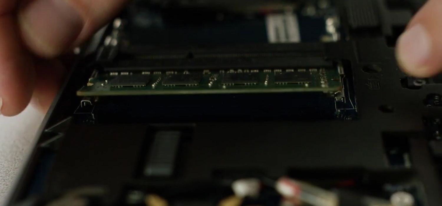 Una persona toglie le clip laterali di un modulo RAM Crucial per rimuoverlo da un portatile